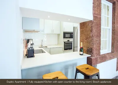 a kitchen with white cabinets and wooden stools at Cayres Suites Surdo in Funchal