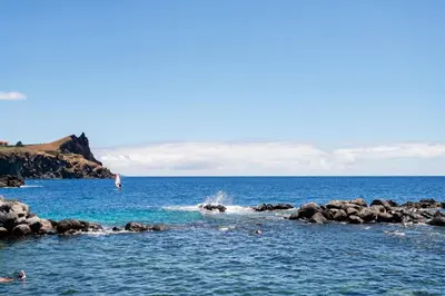 a group of people swimming in the ocean near rocks at Reis Magos II by An Island Apart in Caniço