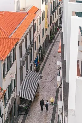 two people walking down a street between buildings at FAA Rentals 31 de Janeiro by An Island Apart in Funchal