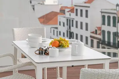 a white table with a plate of fruit on a balcony at FAA Rentals 31 de Janeiro by An Island Apart in Funchal