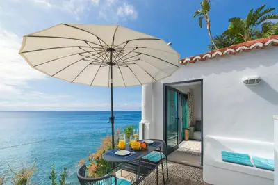 a table with an umbrella next to the ocean at OurMadeira - Cottage do Mar in Arco da Calheta