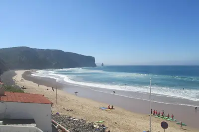 a beach with people sitting on the sand and the ocean at Villa Bartoni in Aljezur