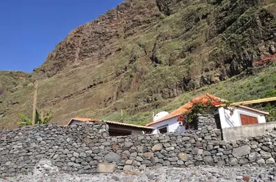 a house with a stone wall and a mountain at Faja dos Padres in Ribeira Brava
