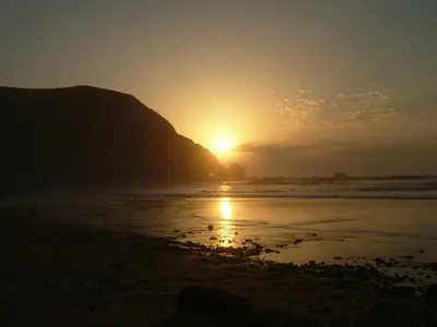 a sunset on the beach with a mountain in the background at Cantinho da Avó in Vila do Bispo