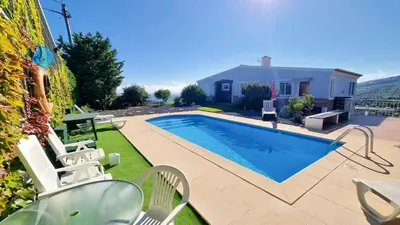 a swimming pool with chairs and a house at Loreto Rose, Panoramic Ocean and Mountain View in Arco da Calheta