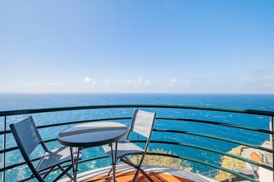 a balcony with chairs and a table and the ocean at Sea View - By WeHost in Câmara de Lobos