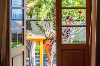 a woman sitting at a table outside a door at Vila Botânica - By WeHost in Funchal