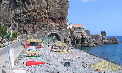 a beach with umbrellas and people on the water at Casa Alto Santo António in Ponta do Sol