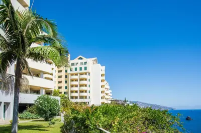 a large white building with the ocean in the background at Falesia Apartment by LovelyStay in Funchal