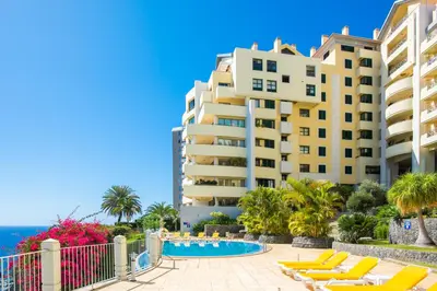 a view of a building and a swimming pool with lounge chairs at Falesia Apartment by LovelyStay in Funchal