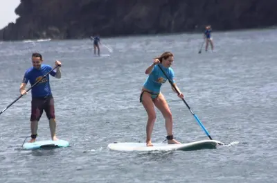 a man and a woman on paddle boards in the water at Ohana Madeira Guest House in Porto da Cruz