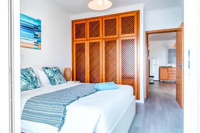 a bedroom with a white bed with a wooden cabinet at Casa Serena Apartments in Arco da Calheta