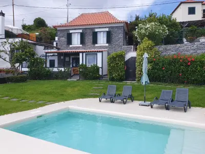 a pool with two chairs and an umbrella and a house at Casa Velha D Fernando e Casa Avó Augusta in Ribeira Brava