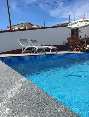 a swimming pool with two chairs and an umbrella at Vila do Rocha in Calheta
