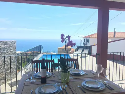 a table with plates and wine glasses on a balcony at Vila do Rocha in Calheta