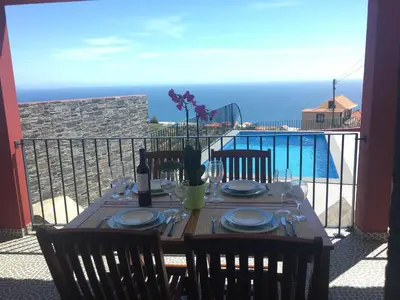 a table with plates and glasses on a balcony with the ocean at Vila do Rocha in Calheta