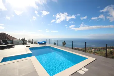 a pool with chairs and an umbrella and the ocean at Villa Por do Sol in Estreito da Calheta