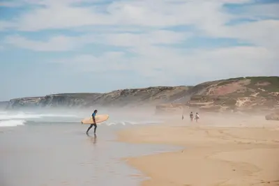 a man walking on the beach with a surfboard at Casa Lusco Fusco in Carrapateira