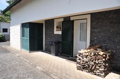 a building with green doors and a pile of wood at Luxury VILLA CAMÉLIA. Mountains, golf, horses, levada walks. in Santo da Serra
