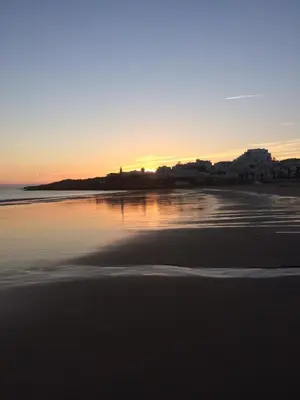 a beach with the sun setting on the water at H&H seaview in Luz