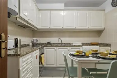 a kitchen with white cabinets and a table with chairs at Apartamento Netos - By WeHost in Funchal