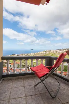 a red chair sitting on a balcony overlooking the ocean at Casa Por Do Sol in Ponta do Sol