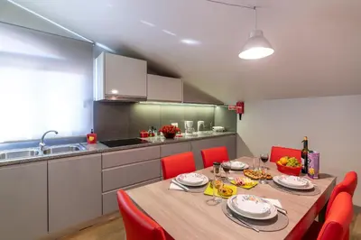 a dining room table with red chairs and a kitchen at Casa Por Do Sol in Ponta do Sol