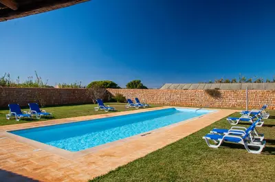 a swimming pool with lounge chairs and a brick wall at Tonel Apartamentos Turisticos in Sagres