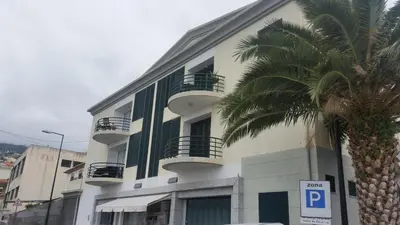 a white building with balconies and a palm tree at Apartment in Câmara de Lobos in Câmara de Lobos