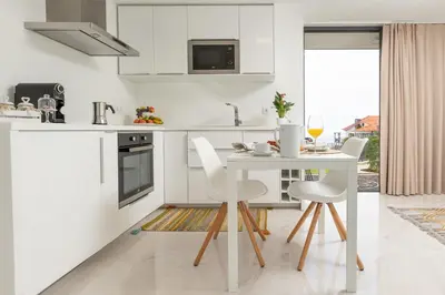 a white kitchen with a white table and chairs at BHF Residences Lotus in Calheta