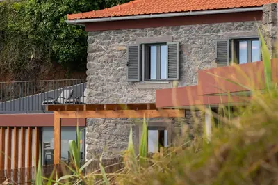 a stone house with black windows and a balcony at BHF Residences Ying Yang in Calheta