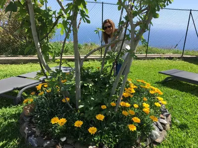 a woman is standing next to a flower garden at La Casa de la Abuela in Ponta do Sol