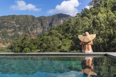 a woman in a hat sitting in a pool looking at a mountain at Casas do Lanço by An Island Apart in São Vicente