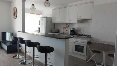 a kitchen with white cabinets and bar stools at Portinho II-Modern apt with balcony facing the sea in Caniço