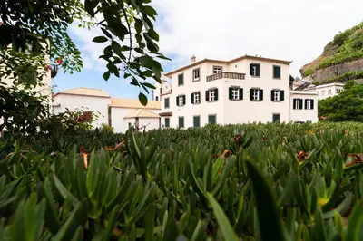 a large white house with a grass field in front of it at Villa Ponta do Sol Apartment in Ponta do Sol