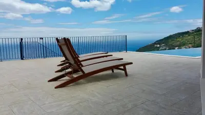 a wooden bench sitting on a patio overlooking the ocean at Villa Palheiros in Arco da Calheta