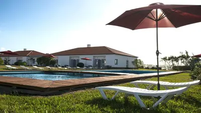 a bench with an umbrella next to a swimming pool at Hotel Santa Maria in Vila do Porto