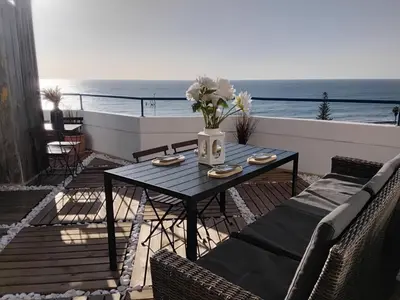 a table with a vase of flowers on a balcony at AMAZING PENTHOUSE- panoramic sea view & tikki bar on private terrasse in Luz