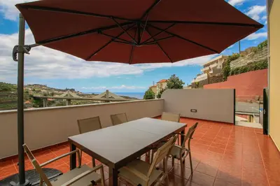 a table and chairs on a balcony with an umbrella at Villas Quinta da Lapa by AnaLodges in Câmara de Lobos