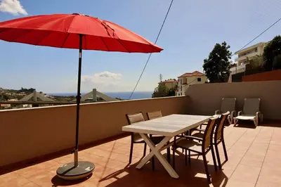 a table and chairs with a red umbrella on a balcony at Villas Quinta da Lapa by AnaLodges in Câmara de Lobos
