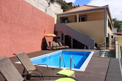 a swimming pool with two chairs and a house at Villas Quinta da Lapa by AnaLodges in Câmara de Lobos