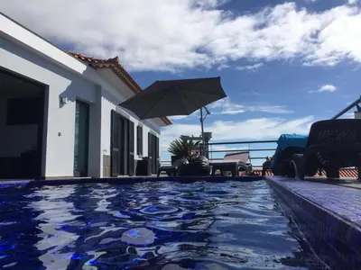 a swimming pool with an umbrella next to a house at Casa Lira in Arco da Calheta