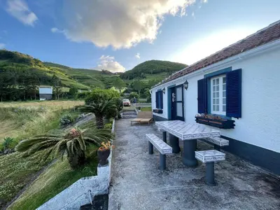 a picnic table outside of a house with mountains in the background at Quinta do Monte Santo in Vila do Porto