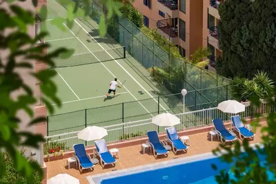 a man playing tennis on a tennis court with chairs and umbrellas at Dorisol Mimosa Studio Hotel in Funchal