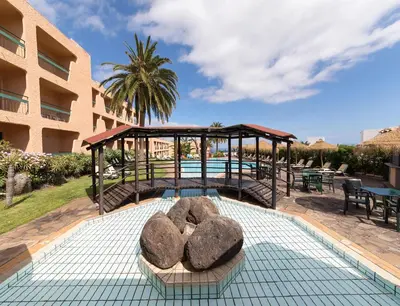 a swimming pool with a gazebo and some rocks at Dom Pedro Garajau in Caniço