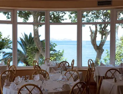 a dining room with white tables and chairs and windows at Dom Pedro Madeira in Machico