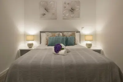a white bed with a bouquet of purple flowers on it at ANGEL´S SUNSET in Estreito da Calheta