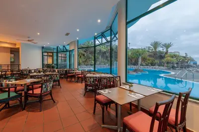 a restaurant with a pool and tables and chairs at Pestana Ocean Bay Resort in Funchal