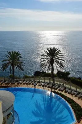 a swimming pool with chairs and palm trees and the ocean at Pestana Grand Ocean Resort Hotel in Funchal