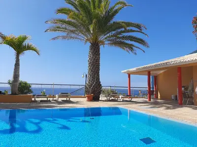 a swimming pool with palm trees and the ocean at Hotel Cais da Oliveira in Caniço